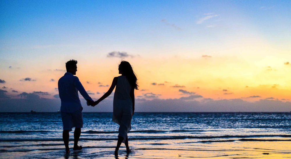 couple on the beach holding hands in the shadows near sunset