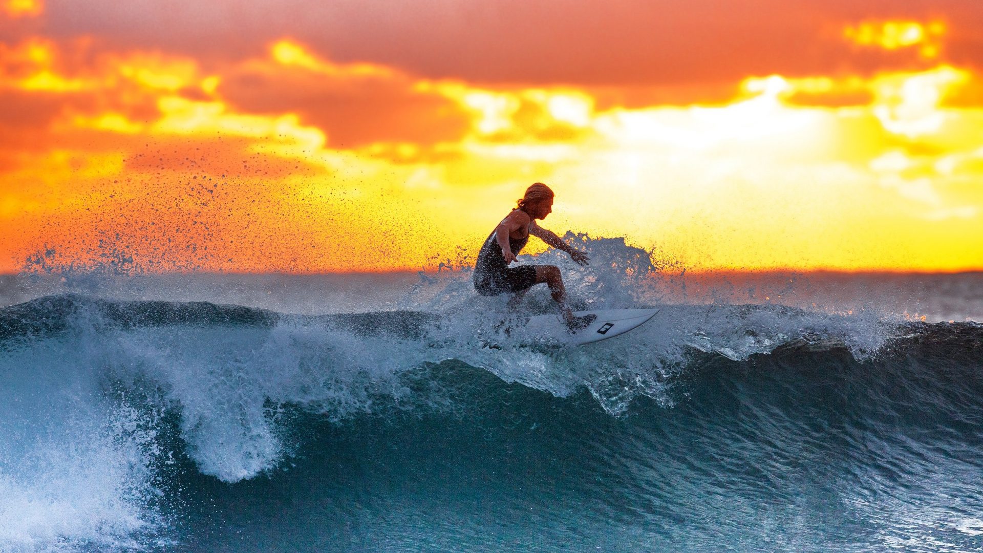 man riding wave on surf board in front of sunset