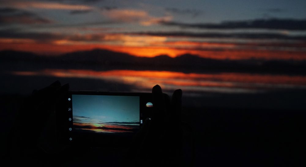 silhouette photography of person capturing sunset with smartphone